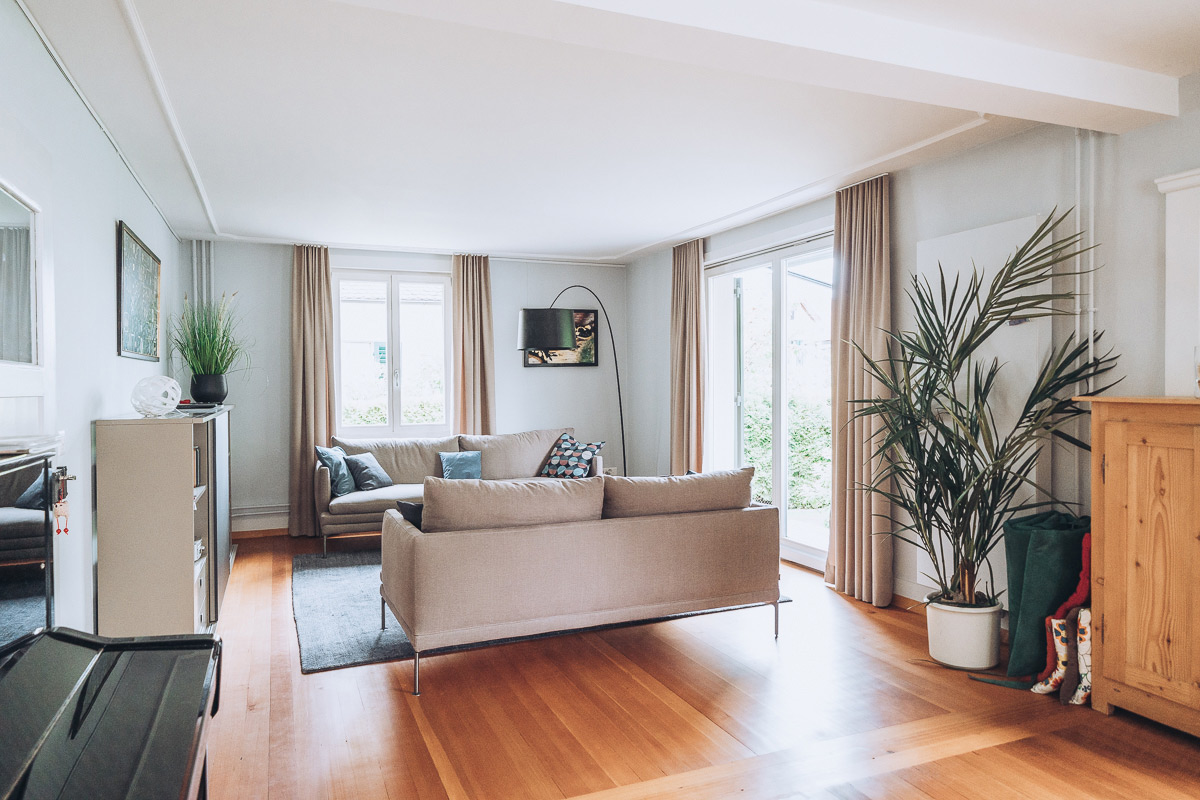 Ansicht einer Wohnungseinrichtung mit Holzm&ouml;beln, gepolstertem Sofa und Vorh&auml;ngen